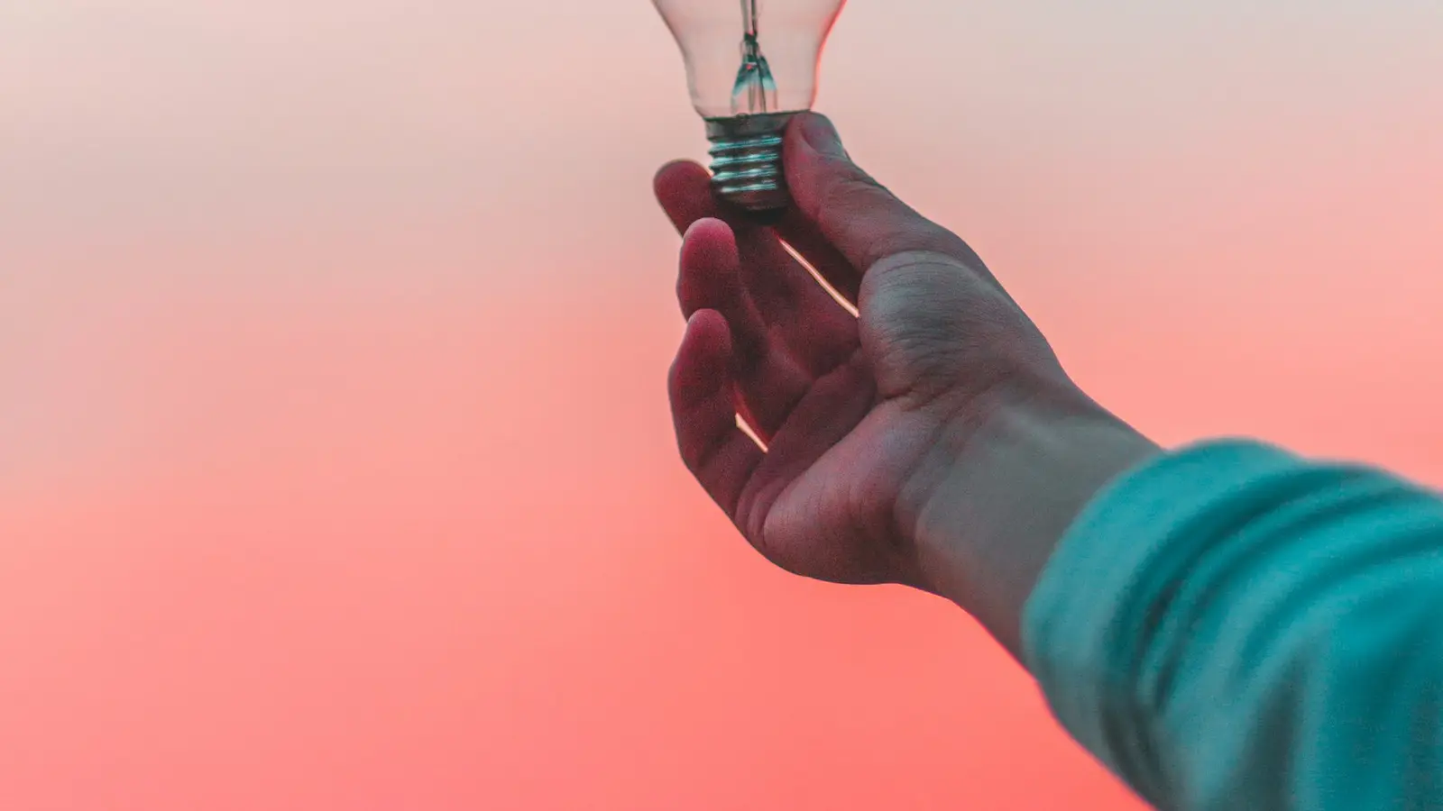 Hand holding a glowing light bulb against a sunset